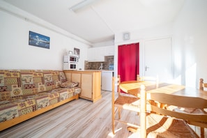 A compact living space with a sofa, dining table, and kitchen area. - L'Ourson - Studio avec balcon plein sud (Les Angles)