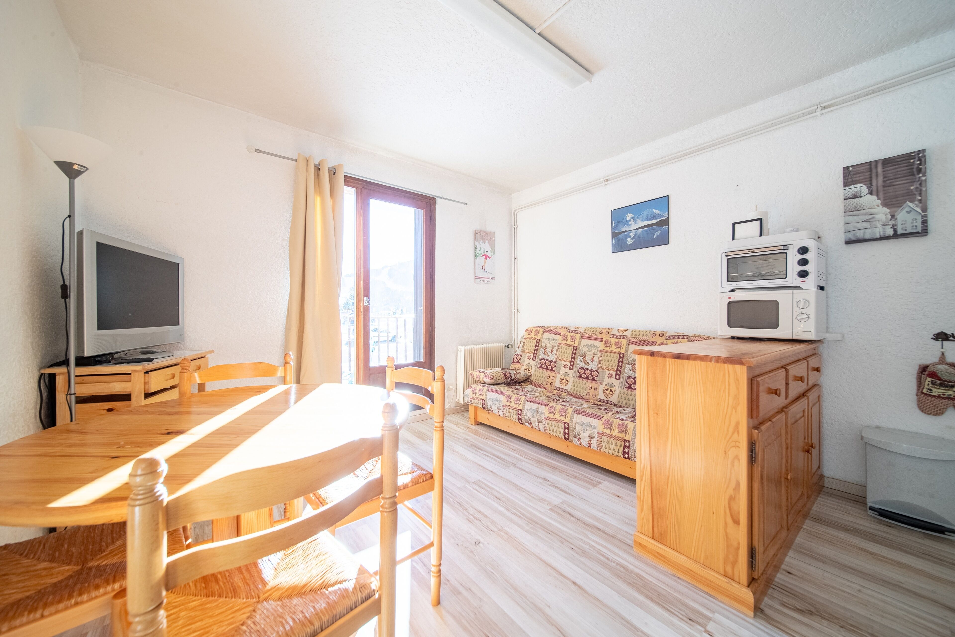 Uma sala de estar com mesa de jantar de madeira, cadeiras, sofá, televisão e micro-ondas.