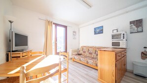 Un salon comprenant une table à manger en bois, des chaises, un canapé, un téléviseur et un four à micro-ondes.
