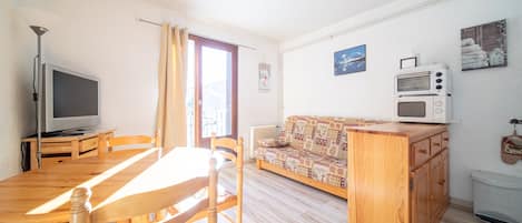 Uma sala de estar com mesa de jantar de madeira, cadeiras, sofá, televisão e micro-ondas.