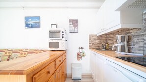 Une cuisine compacte dotée d’armoires en bois, d’un four à micro-ondes, d’une machine à café et d’une poubelle.