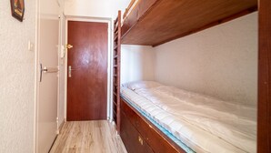 Un couloir étroit avec une porte en bois et un lit superposé avec un matelas.