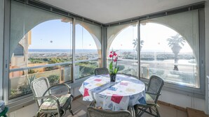 Un balcón con una mesa redonda, sillas y un florero con flores.