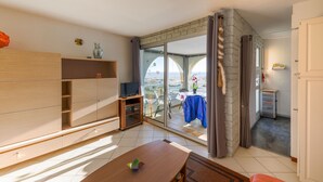 Una sala moderna con un mueble de entretenimiento de madera, una mesa de comedor y un amplio ventanal corredero que da a un balcón.