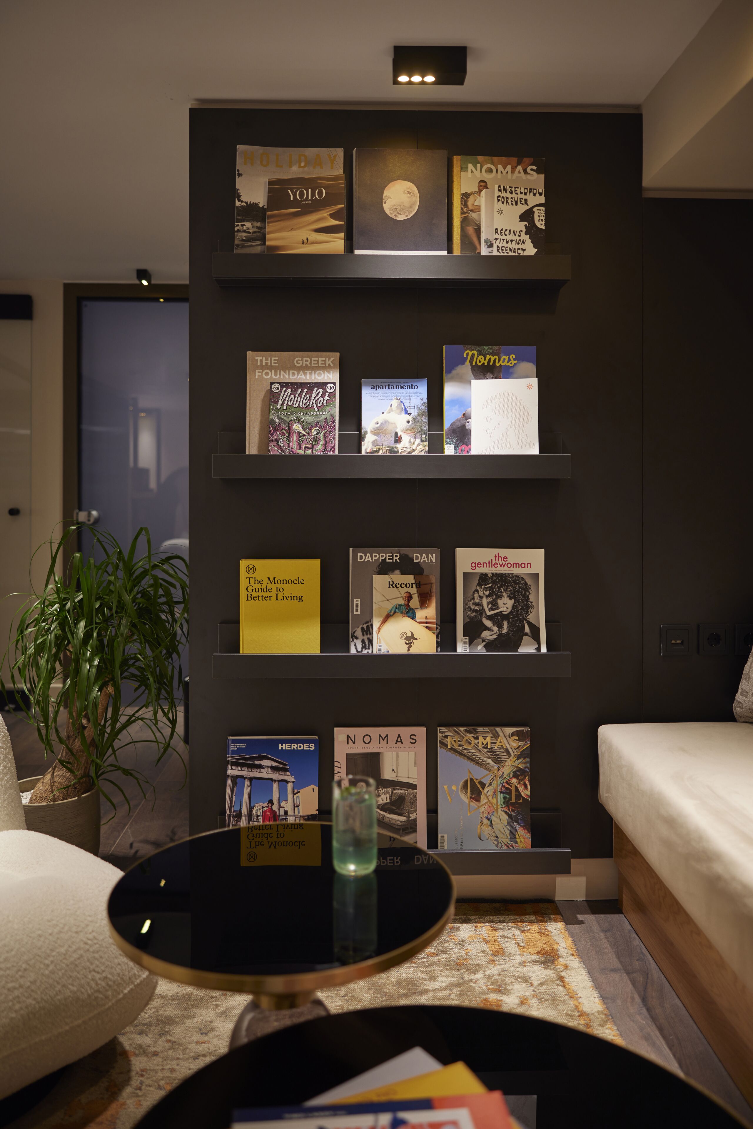 A modern living room with a bookshelf displaying various books, a round coffee table, and a potted plant.
