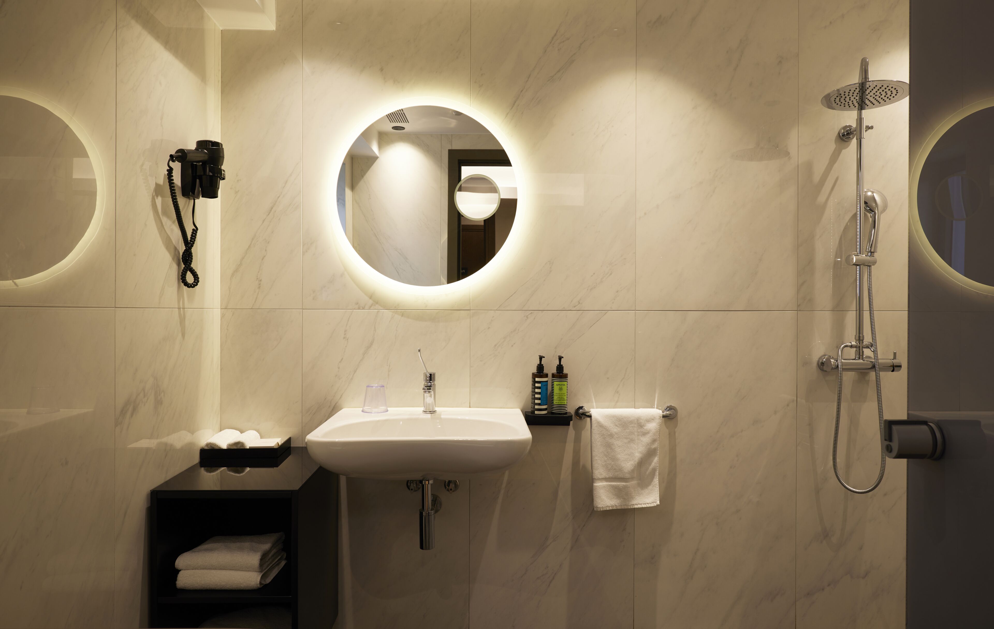Un baño moderno con un espejo redondo, un lavabo y una ducha.