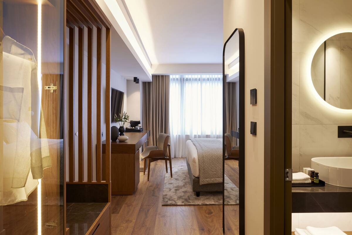 Quarto de hotel moderno com uma escrivaninha de madeira, uma cama confortável, um espelho grande e um banheiro com banheira.