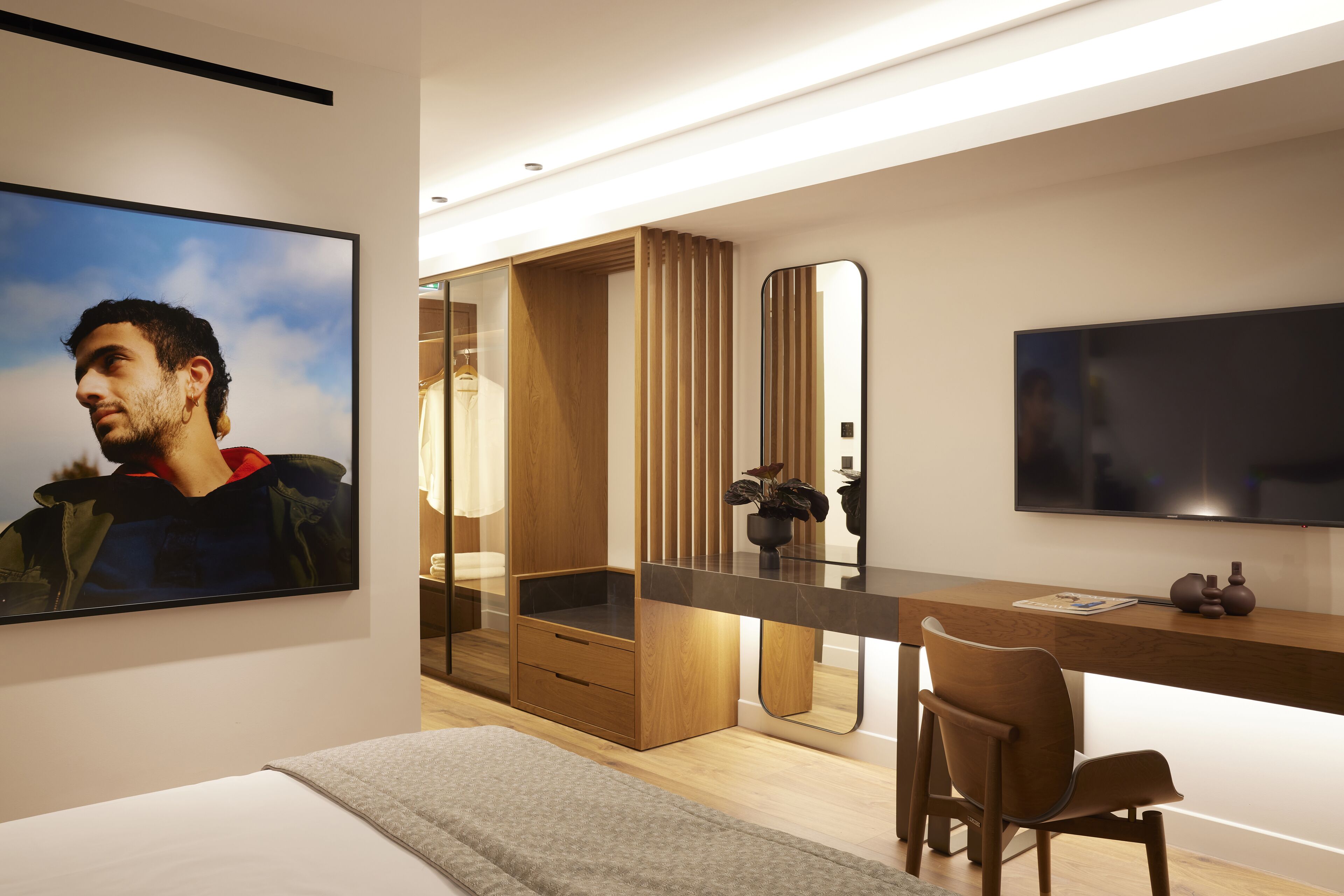 Habitació d'hotel moderna amb llit, escriptori amb cadira, un mirall gran i televisió de pantalla plana.