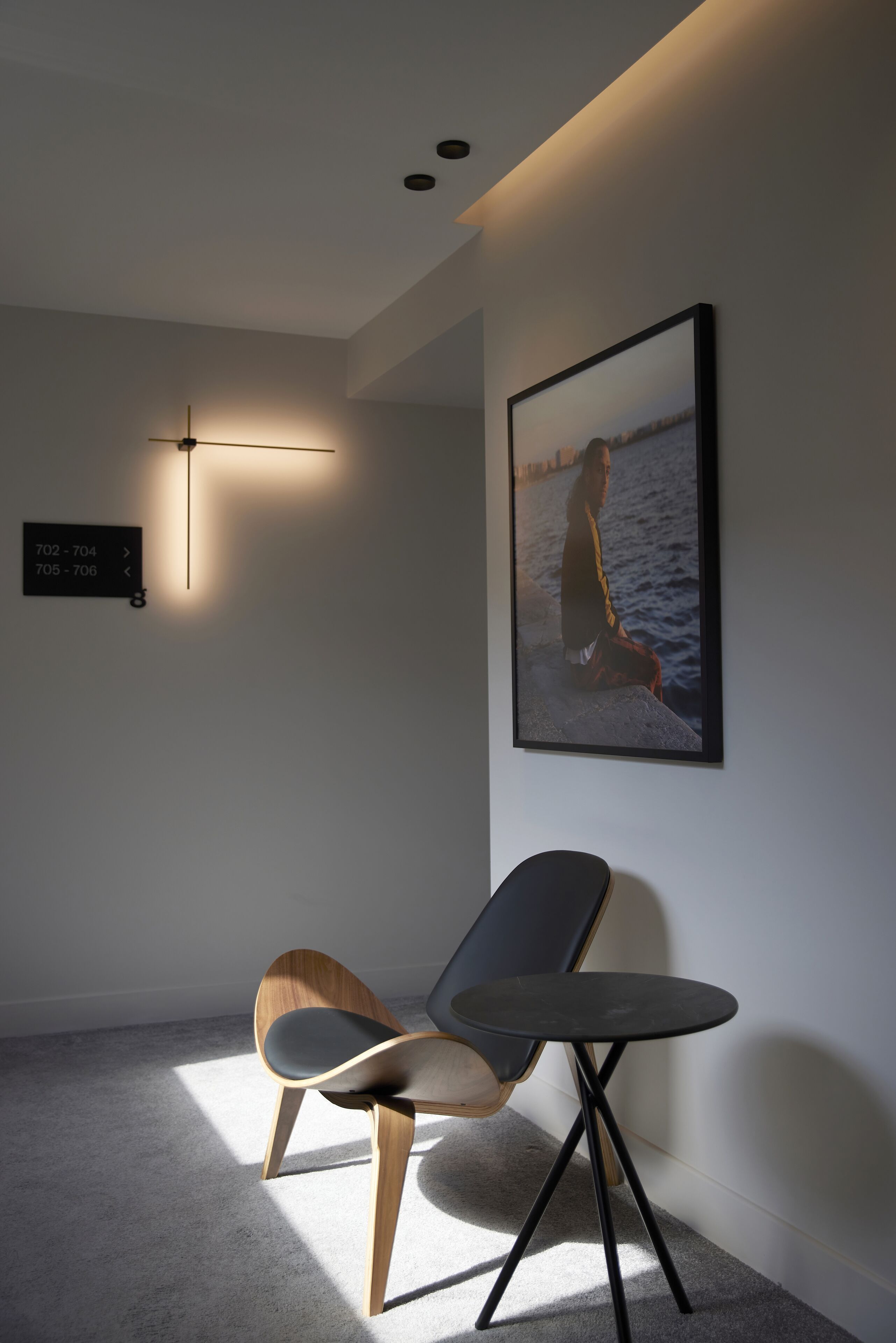 Ein modernes Zimmer mit einem Sessel und einem kleinen Tisch, einem gerahmten Bild an der Wand und einem Hinweisschild.