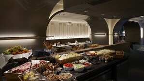 A buffet with various food items and a seating area with tables and chairs.