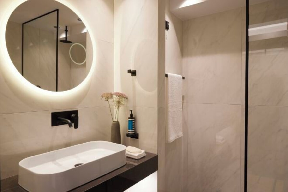 Un baño moderno con una bañera independiente, un espejo redondo y una cabina de ducha de vidrio.