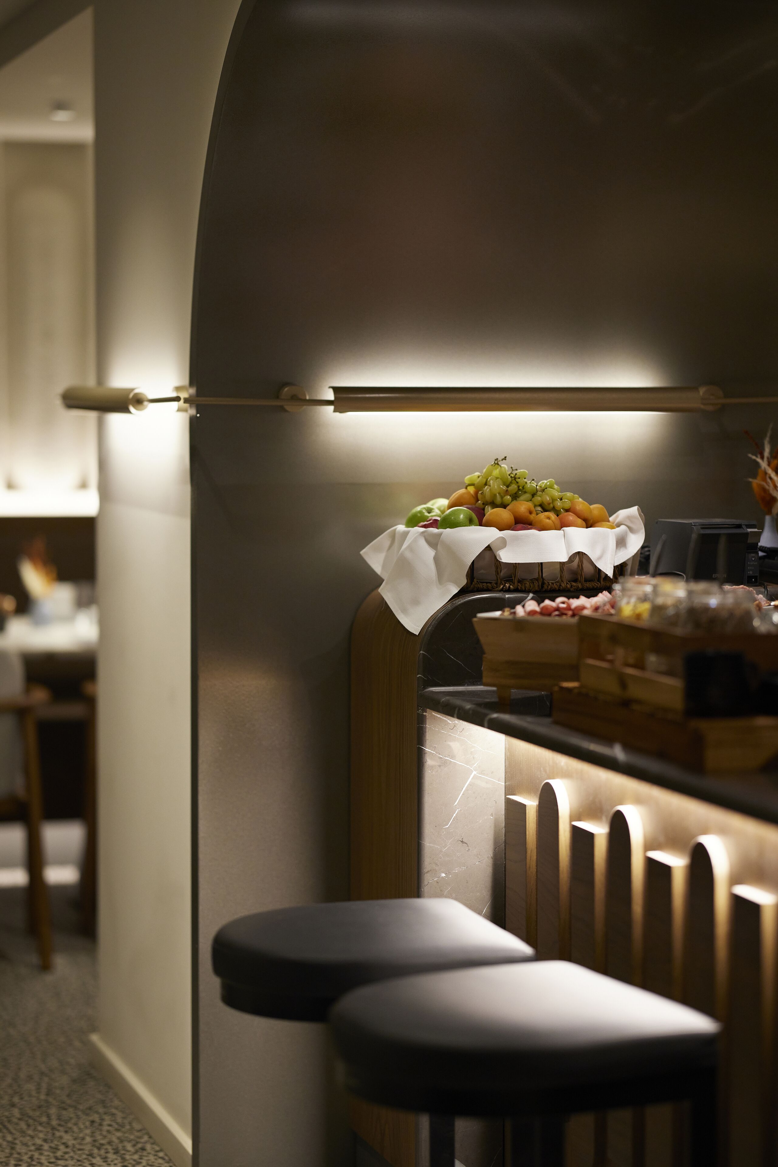 A kitchen area with a fruit display, bar stools, and a modern countertop.