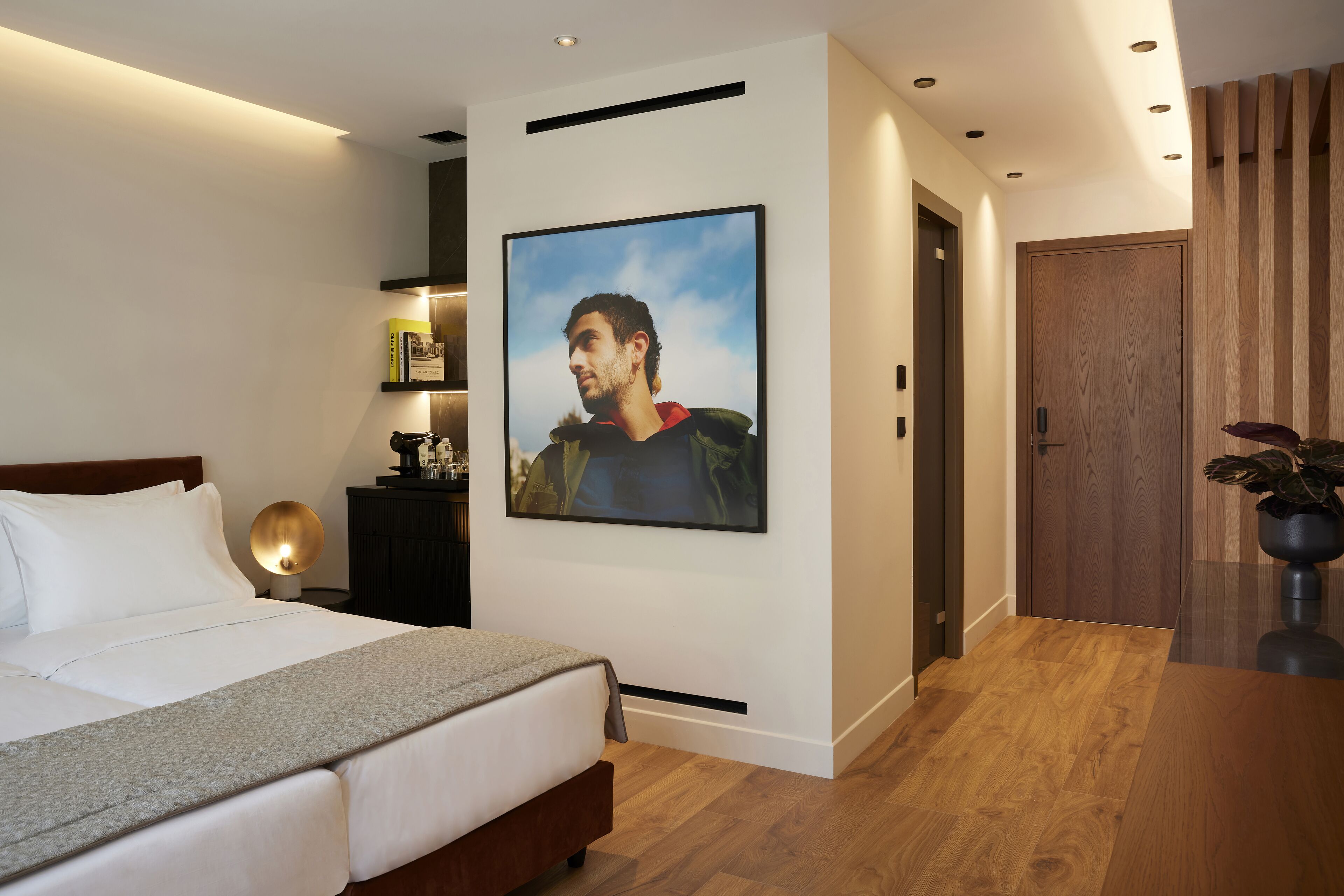 Un dormitorio moderno con una cama grande, un cuadro en la pared, una mesita de noche con lámpara y suelo de madera.