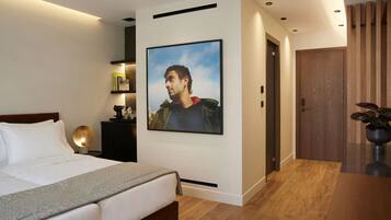 A modern bedroom with a large bed, a wall-mounted picture, a bedside table with a lamp, and a wooden floor.