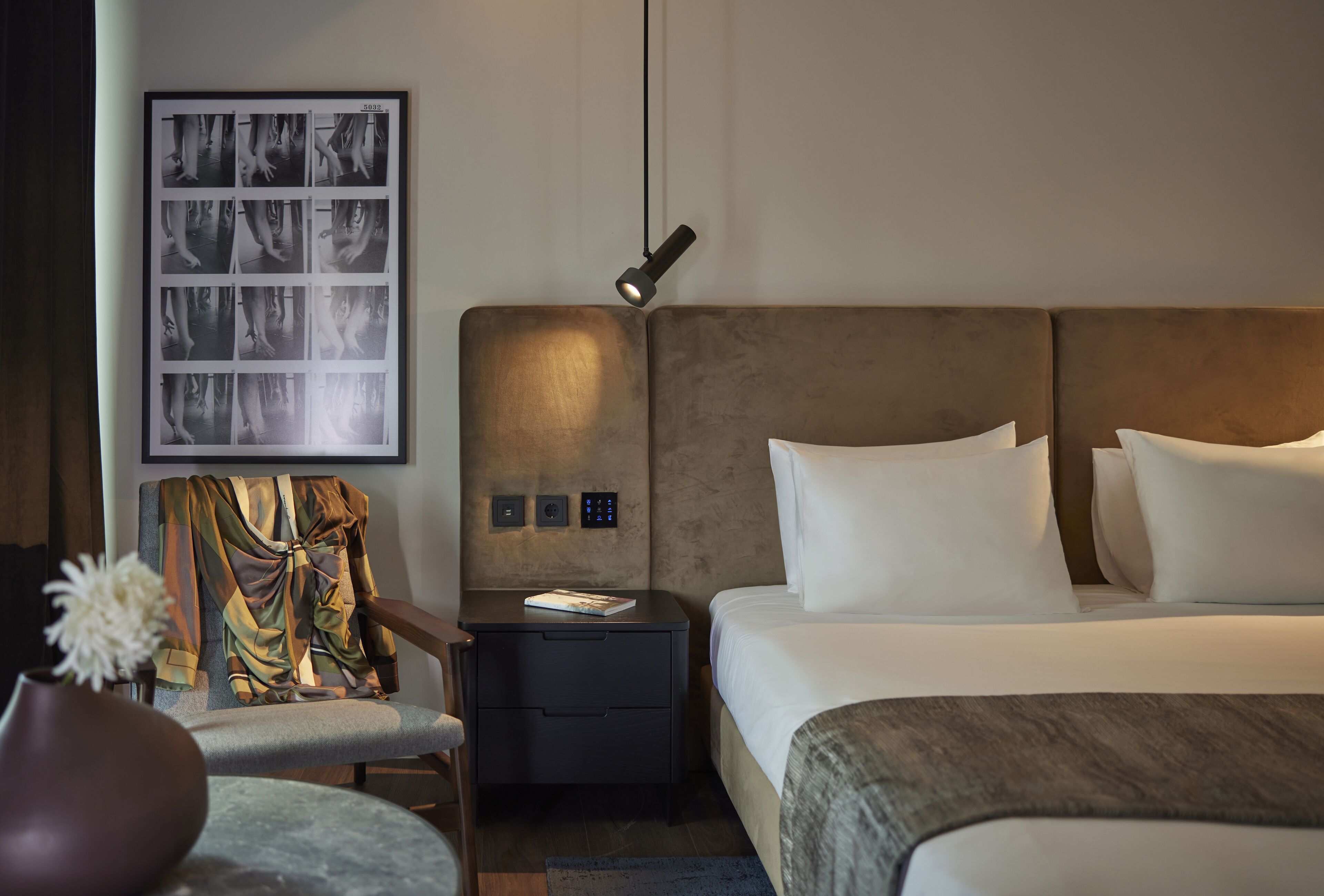 Una camera d'albergo moderna con un letto grande, un comodino, una sedia e un'opera d'arte appesa al muro.