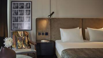 Una camera d'albergo moderna con un letto grande, un comodino, una sedia e un'opera d'arte appesa al muro.