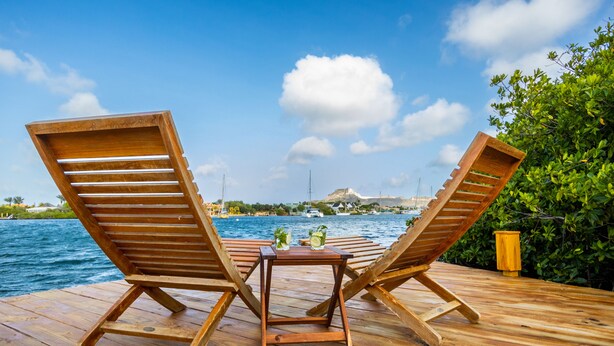 Deux fauteuils en bois, placés face à une étendue d’eau, avec une petite table entre eux.