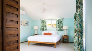 Une chambre à coucher avec un lit, deux tables de chevet avec des lampes, un ventilateur de plafond et une fenêtre avec des rideaux.