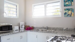 Une cuisine dotée de plans de travail en granit, de meubles blancs, d’une cuisinière à gaz, d’un four à micro-ondes, d’une machine à café et de deux fenêtres équipées de stores.