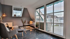 A modern living room with a large window, a sofa, a coffee table, and a lamp.