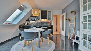 A modern kitchen with a round dining table, grey chairs, and a hanging light fixture.