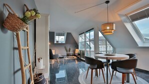 A modern loft bedroom with a skylight, a dining area with a round table, and a large window offering a view.