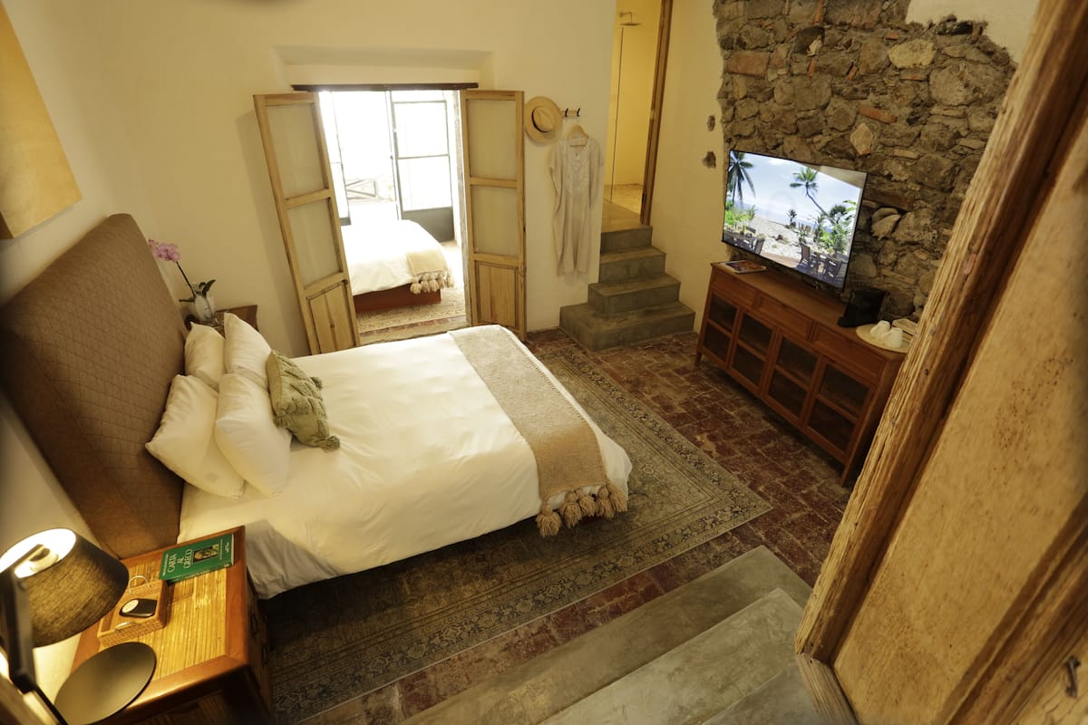 Ein Schlafzimmer mit Bett, Fernseher, Holzschrank, Spiegel und Treppe.