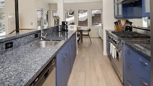 Een moderne keuken met granieten aanrechtbladen, roestvrijstalen apparatuur en blauwe kastjes.