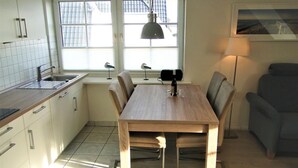 Et moderne køkken med hvide skabe, et træspisebord og et vindue med udsigt til bygninger.