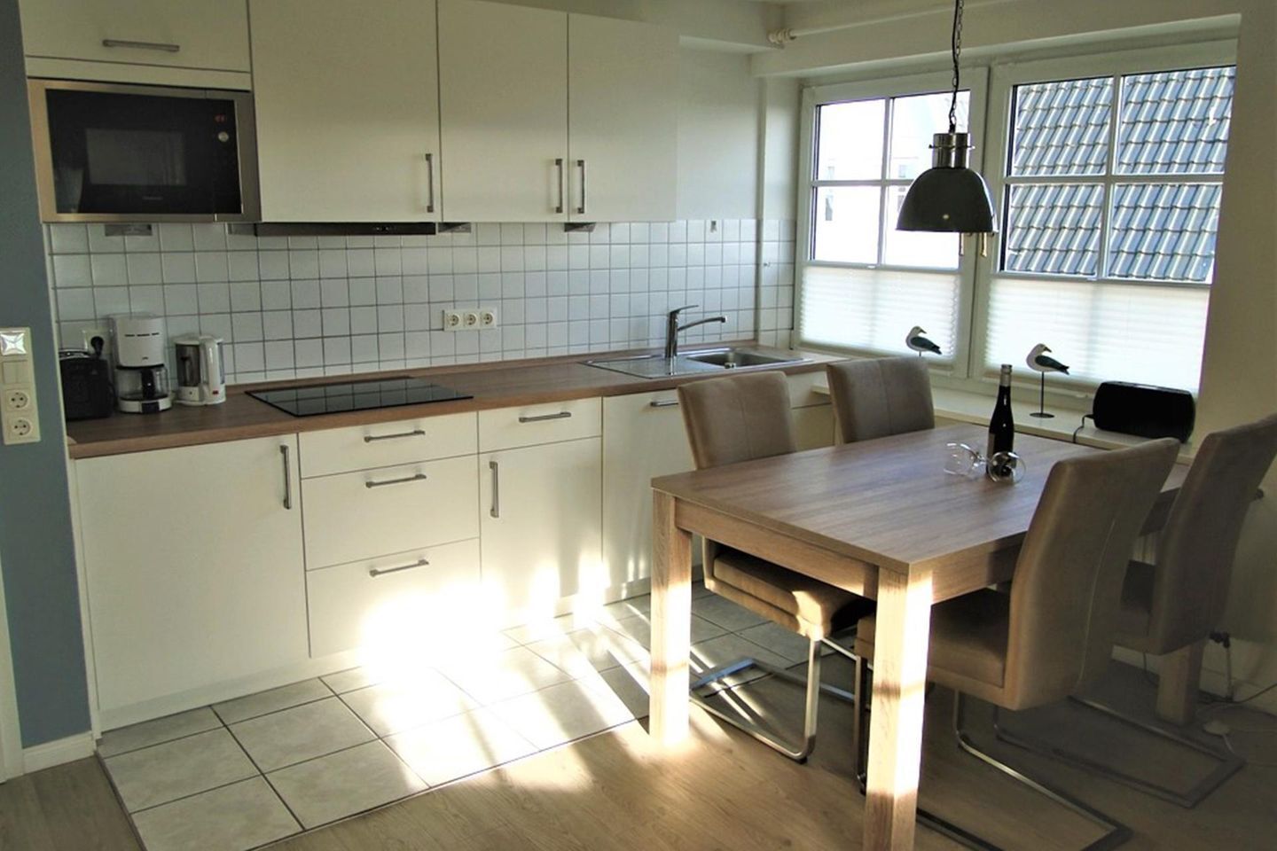 A compact kitchen with white cabinets, a microwave, a sink, and a dining area with a table and chairs.