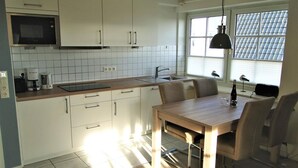 Et kompakt køkken med hvide skabe, en mikrobølgeovn, en vask og et spiseområde med et bord og stole.