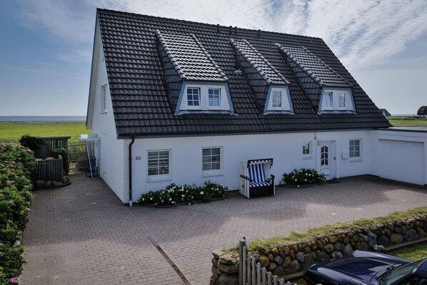 A white house with a black tiled roof, numbered 33, featuring a small porch and a chair.