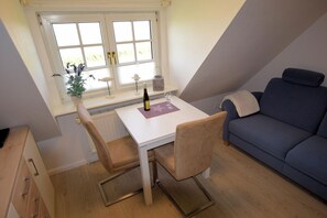 Une petite pièce agréable, avec une table blanche, deux chaises, un canapé bleu et une fenêtre donnant sur un paysage verdoyant.
