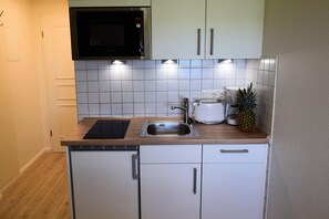 A compact kitchen with white cabinets, a built-in microwave, a toaster, and a sink. - Hüs Thora Jaiken "App.Birthe" TJ/02 - Thora Jaiken (Sylt)