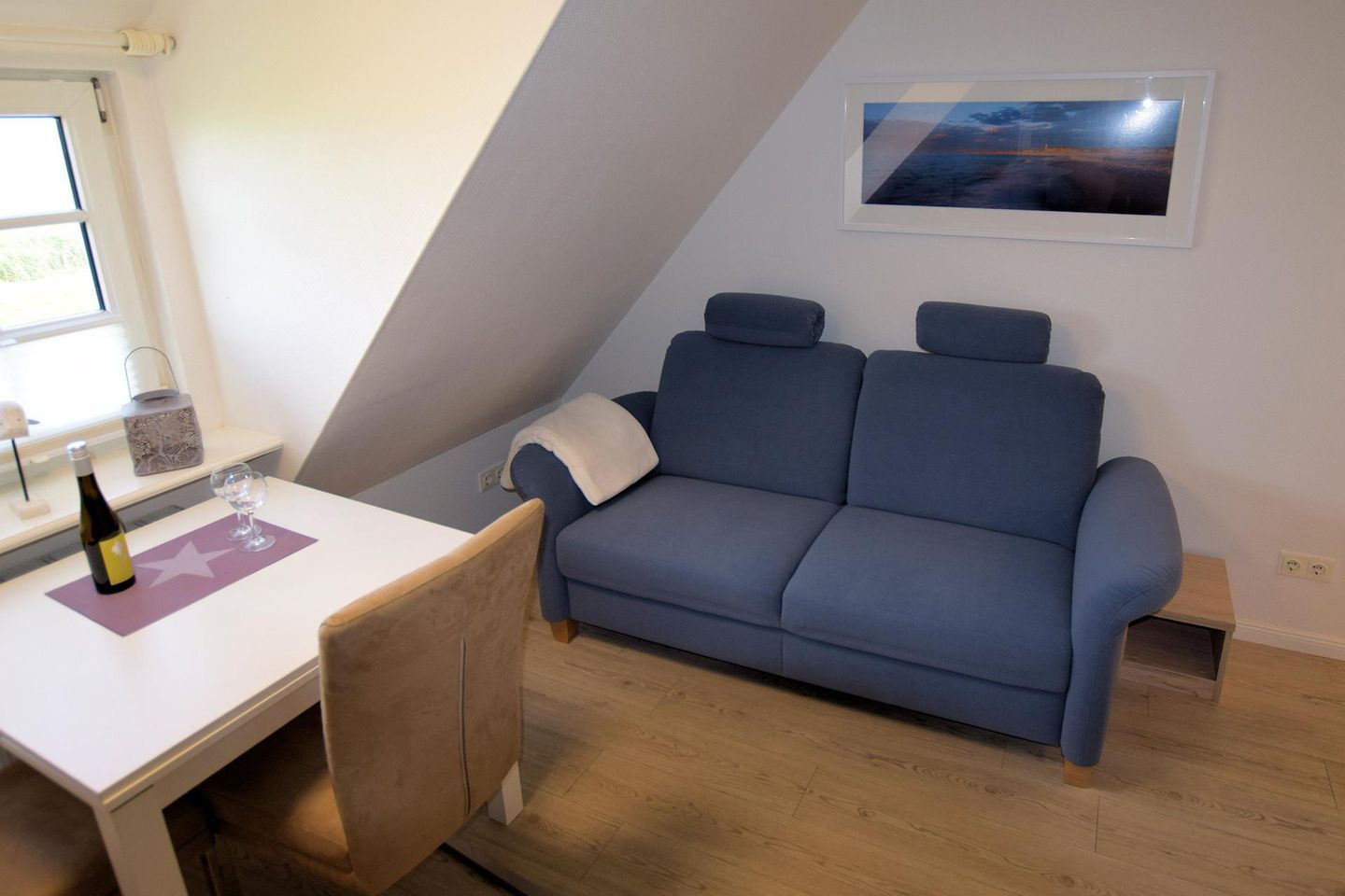 A room with a blue sofa, a small table with a bottle and glass, and a framed picture on the wall.