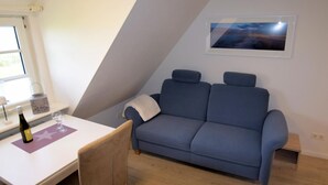 Ein Zimmer mit einem blauen Sofa, einem kleinen Tisch mit Flasche und Glas sowie einem gerahmten Bild an der Wand.