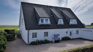 Ein weißes Haus mit schwarzem Schindeldach, Hausnummer 33, mit einer kleinen Veranda und einem Stuhl.