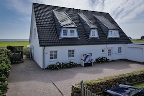 A white house with a black tiled roof, numbered 33, featuring a small porch and a chair. - Hüs Thora Jaiken "App.Birthe" TJ/02 - Thora Jaiken (Sylt)