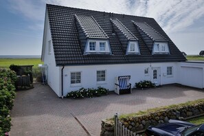 A white house with a black tiled roof, numbered 33, featuring a small porch and a chair. - Hüs Thora Jaiken "App. Eike" TJ/03 - Thora Jaiken (Sylt)