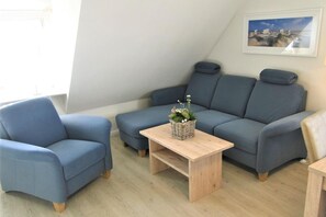 A modern living room with a blue sofa, a matching armchair, and a wooden coffee table. - Hüs Thora Jaiken "App. Eike" TJ/03 - Thora Jaiken (Sylt)