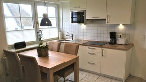 Une cuisine moderne avec un coin repas, comprenant une table en bois, des chaises, un luminaire suspendu noir, un four à micro-ondes, un grille-pain et une machine à café.
