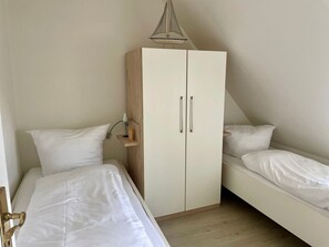 A bedroom with two single beds, a wardrobe, and a hanging light fixture.