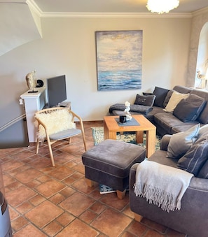 A living room with a sofa, ottoman, chair, coffee table, and a painting on the wall.