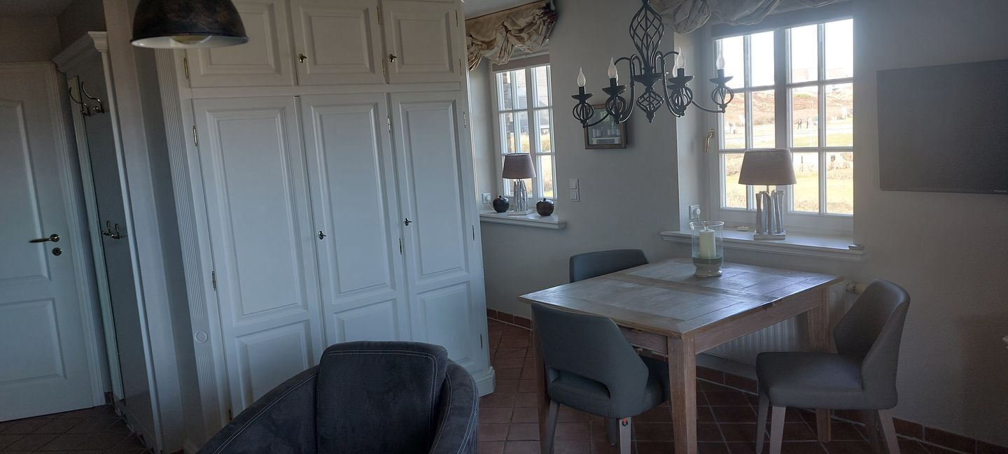 Un espace repas comprenant une table, des chaises, un lustre et une fenêtre avec des rideaux.
