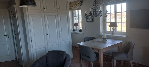 Un espace repas comprenant une table, des chaises, un lustre et une fenêtre avec des rideaux.