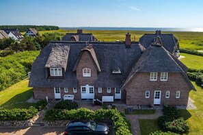 Une grande maison à deux étages, dotée d’un toit à forte pente, de plusieurs cheminées et d’une pelouse bien entretenue.