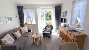 A living room with a sofa, a chair, a small table, a wooden cabinet, and a TV. - Wattstübchen SO/16a - Söl'ring Hüs (Sylt)