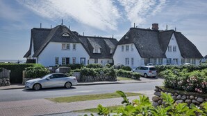 A row of white houses with thatched roofs, a paved driveway, and parked cars. - Wattstübchen SO/16a - Söl'ring Hüs (Sylt)