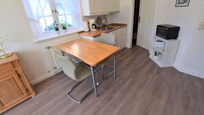 A compact kitchen with a wooden table, white cabinets, a radiator, and a black appliance on the countertop. - Wattstübchen SO/16a - Söl'ring Hüs (Sylt)