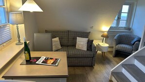 A cozy room with a checkered sofa, a small table with a magazine, a bottle of wine, and a lamp. - Söl'ring Hüs SO/19 - Söl'ring Hüs (Sylt)